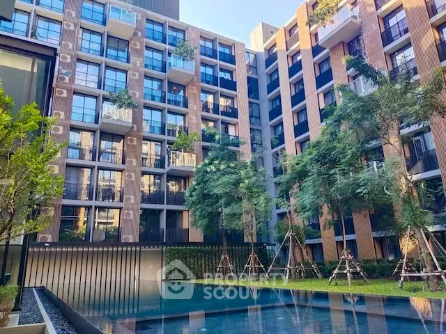 Modern apartment building with pool and lush greenery in urban setting.