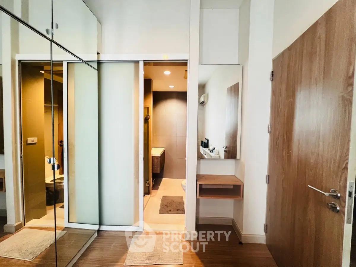 Modern bathroom entrance with mirrored closet doors and wooden accents