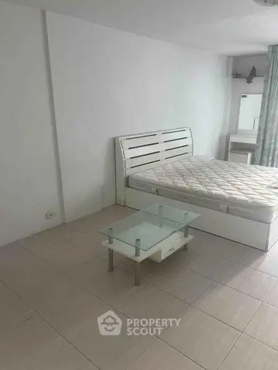 Minimalist bedroom with white bed and glass coffee table in modern apartment.