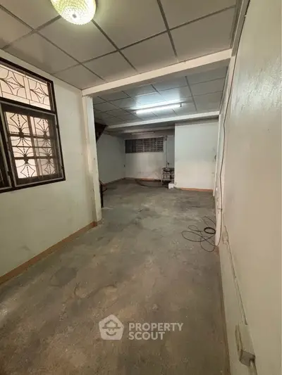 Spacious unfinished room with potential for renovation, featuring tiled ceiling and large window.