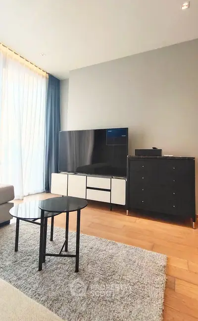 Modern living room with sleek furniture and large TV, featuring natural light and elegant decor.