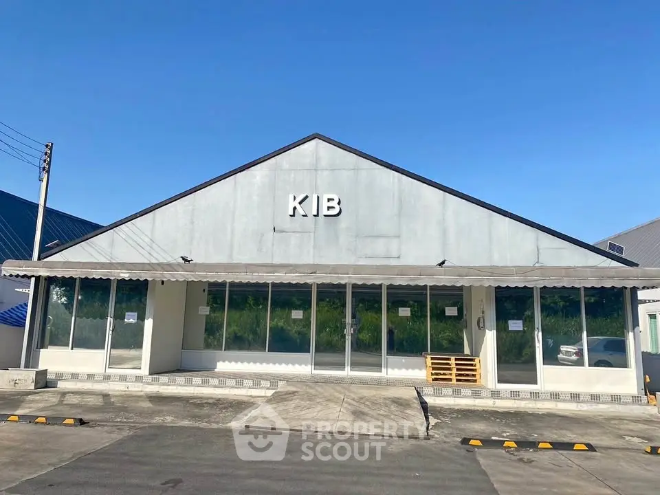 Commercial building exterior with large glass windows and ample parking space.