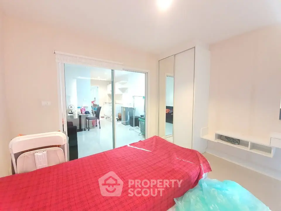 Spacious bedroom with modern furnishings and sliding glass doors leading to a bright kitchen area.