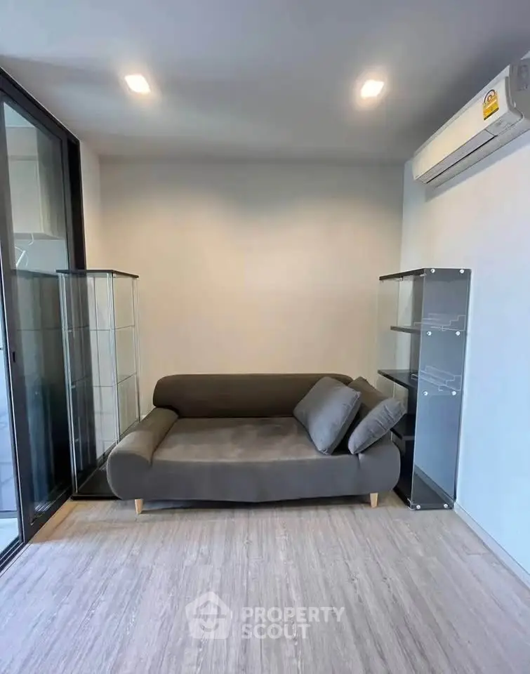 Modern living room with sleek sofa and glass display cabinets, featuring minimalist design and air conditioning.