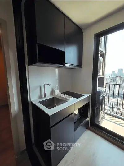 Modern compact kitchen with sleek black cabinetry and balcony view in urban apartment