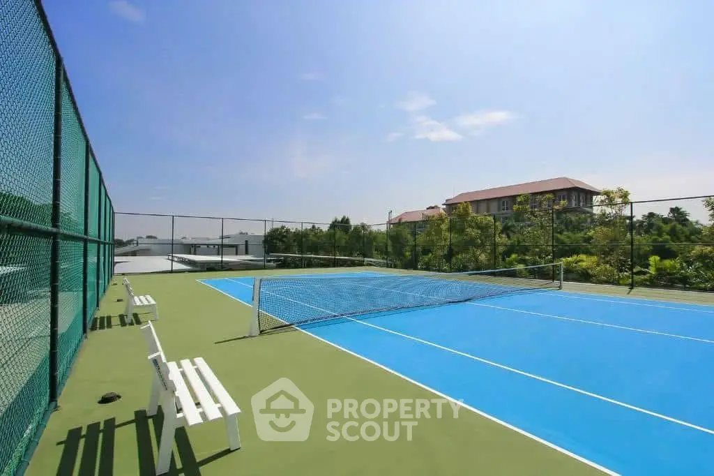 Spacious outdoor tennis court with lush greenery and clear blue sky.