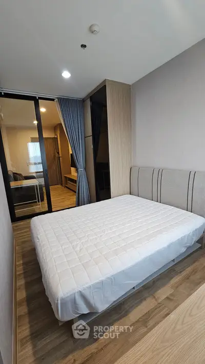 Modern bedroom with stylish decor and wooden flooring, featuring a cozy bed and sliding glass door.