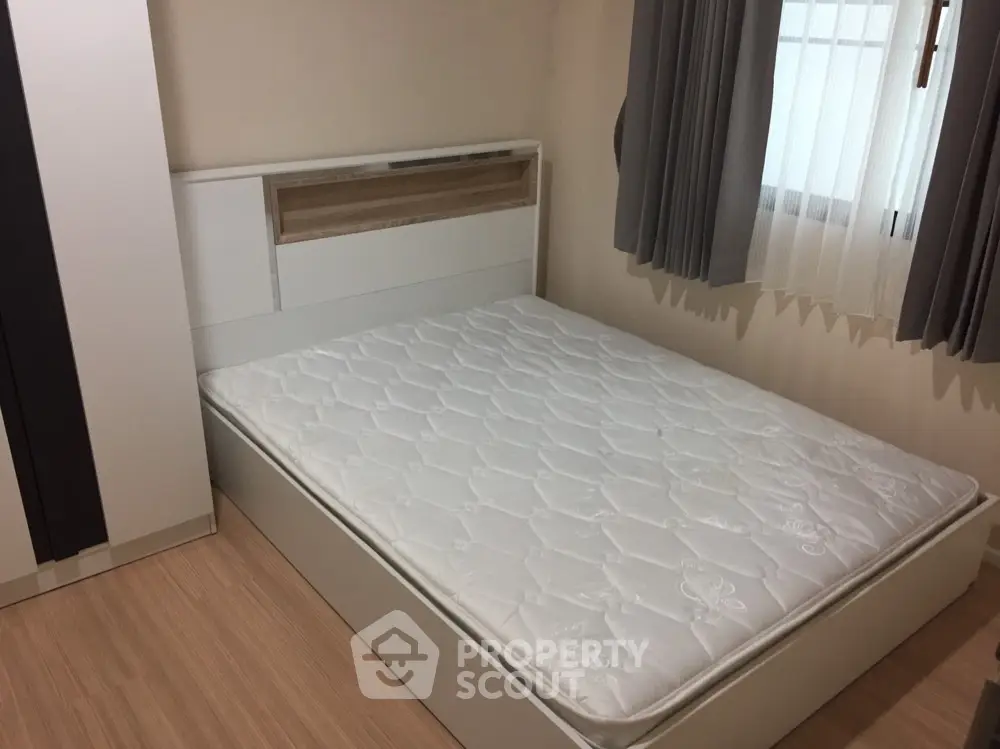 Cozy bedroom with a large window allowing natural light, complemented by elegant curtains and a spacious bed awaiting your personal touch.