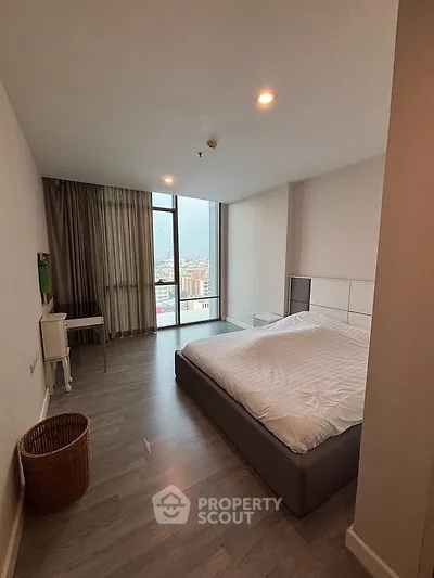 Spacious bedroom with large window offering city views, modern furnishings, and elegant decor.
