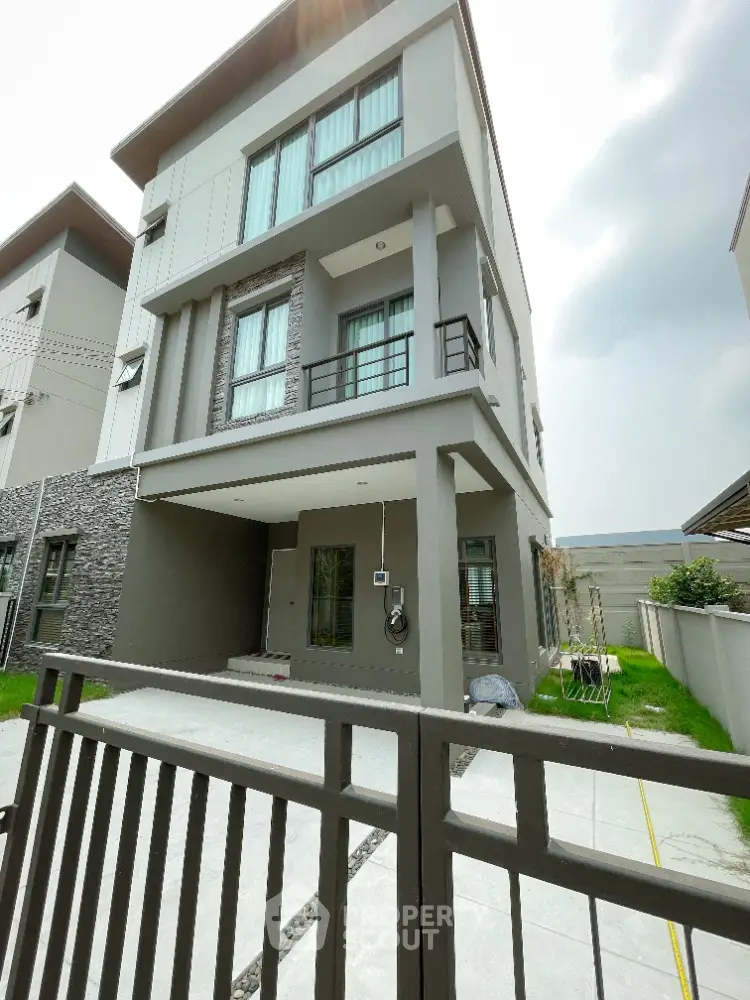 Modern three-story house with stylish facade and gated entrance in suburban neighborhood.