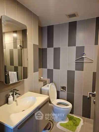 Modern bathroom with sleek design and stylish tiles, featuring a vanity, toilet, and shower area.