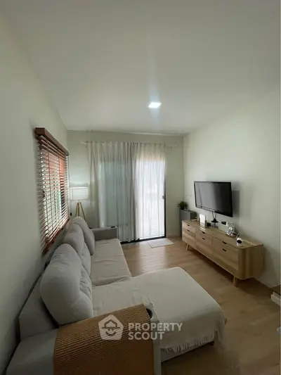 Cozy living room with modern decor, large sofa, TV, and natural light from window and glass door.