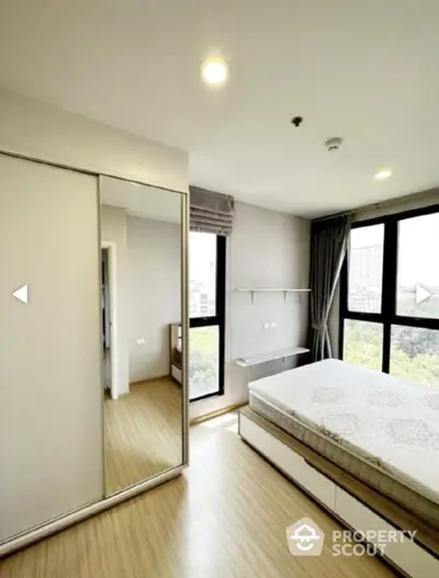 Bright bedroom with large windows and mirrored wardrobe in modern apartment.