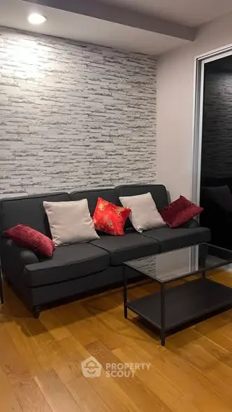 Modern living room with stylish sofa and accent pillows, featuring a chic brick wall and wooden flooring.