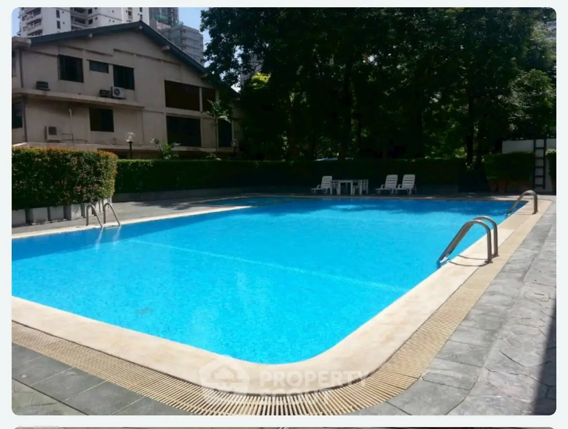 Luxurious residential pool area with pristine blue water and lush greenery, perfect for relaxation and leisure.