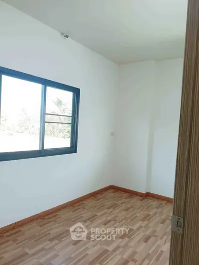 Bright empty room with wooden flooring and large window, perfect for customization.