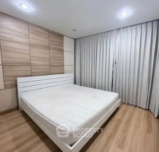 Modern bedroom with wooden flooring and large window draped with curtains.