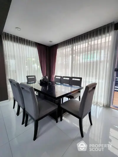 Elegant dining area with modern table and chairs, surrounded by large windows with sheer curtains.