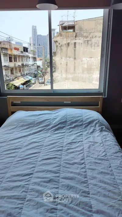 Cozy bedroom with city view through large window, perfect for urban living.