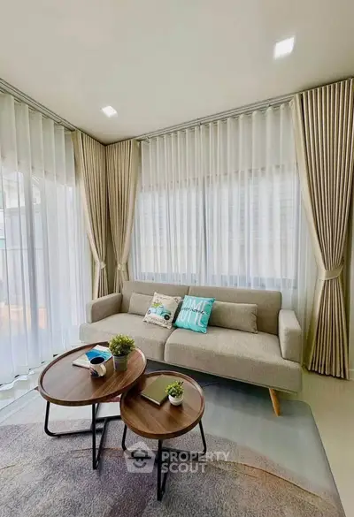 Stylish living room with modern sofa and coffee tables, featuring elegant curtains and natural light.