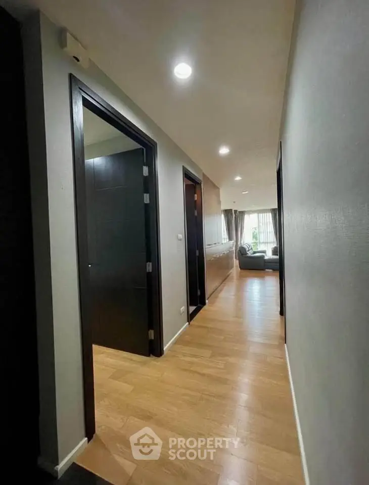 Spacious apartment hallway leading to a bright living room with wooden flooring.