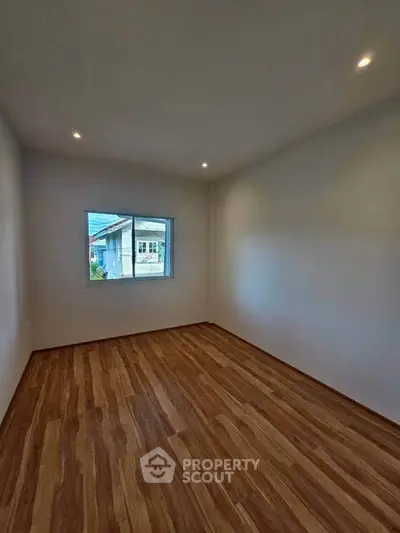 Spacious empty room with wooden flooring and a window view, perfect for customization.