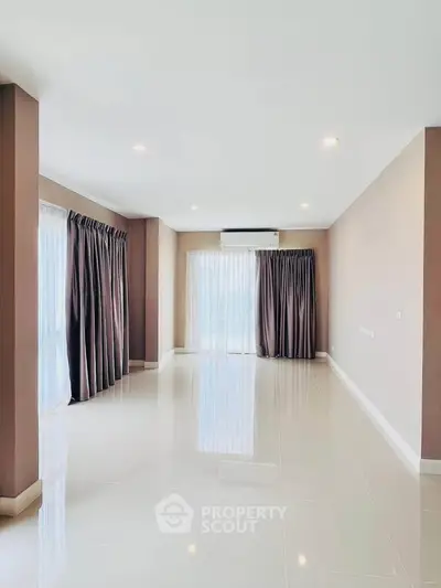 Spacious empty living room with large windows and elegant curtains