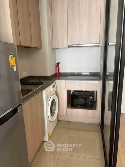 Modern compact kitchen with sleek appliances and wooden cabinetry, featuring a washing machine and built-in oven.