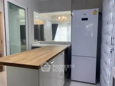 Modern kitchen with sleek white fridge and wooden countertop, featuring open layout and elegant lighting.