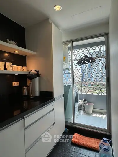 Modern kitchen with balcony and washing machine, sleek cabinets, and city view.