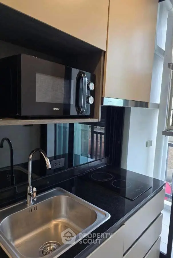 Modern kitchen with sleek black countertop and built-in microwave, featuring a stainless steel sink and electric stove.