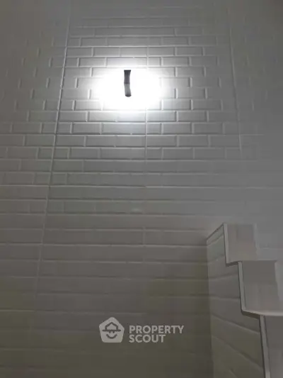 Modern bathroom with sleek white tiles and stylish wall light fixture.