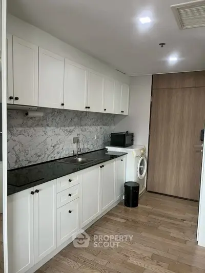 Modern kitchen with sleek cabinets and marble backsplash, featuring a washing machine and microwave.