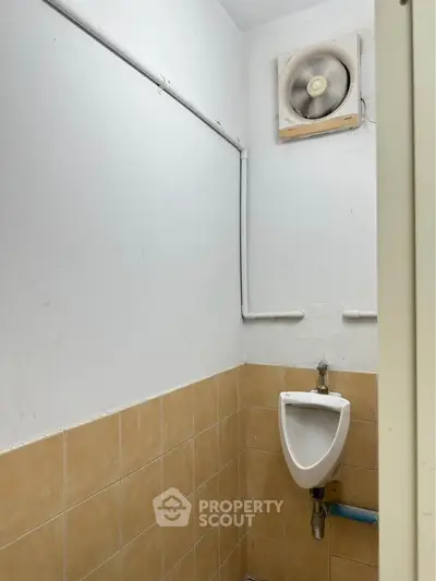 Compact bathroom with urinal and ventilation fan, featuring beige tiles and white walls.