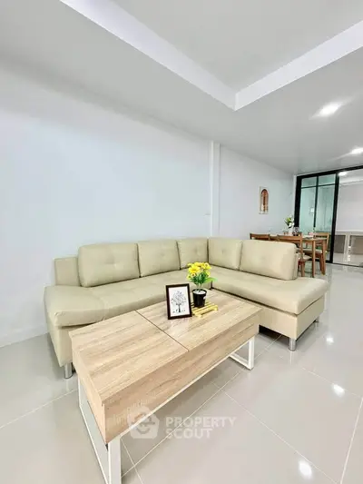 Modern living room with beige sectional sofa and sleek wooden coffee table in a bright, minimalist apartment.