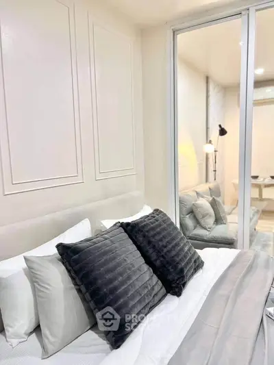 Modern bedroom with plush pillows and sliding glass door to cozy living area.