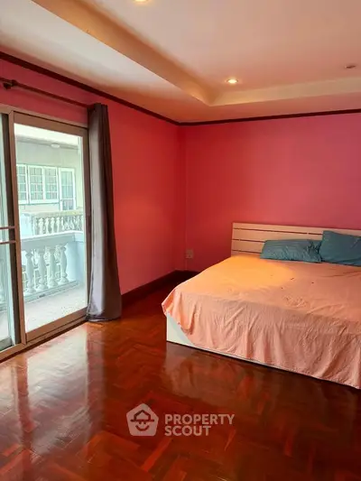 Spacious bedroom with balcony access and wooden flooring in vibrant pink decor.
