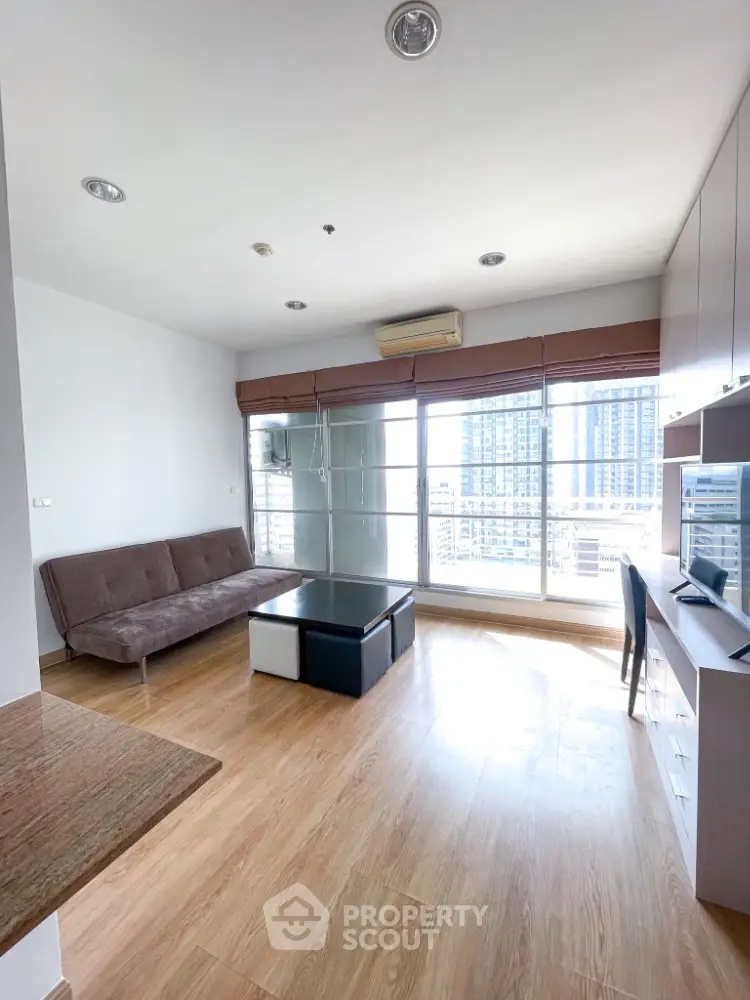 Modern living room with large windows and city view, featuring sleek furniture and wooden flooring.