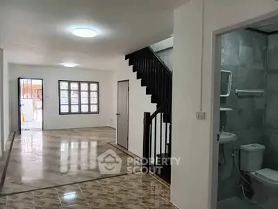 Spacious open-plan living area with staircase and adjacent bathroom, featuring modern tiled flooring.