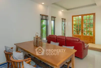 Spacious living room with wooden dining set and red leather sofa, featuring large windows and natural light.
