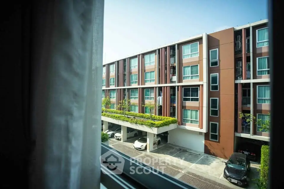 Modern apartment building with parking and greenery viewed from window.