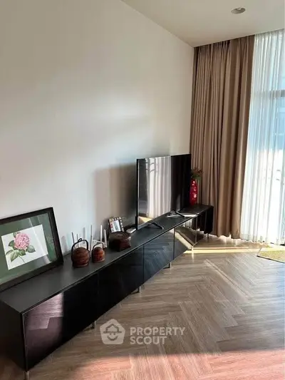 Modern living room with sleek TV stand and elegant decor, featuring floor-to-ceiling curtains and herringbone flooring.