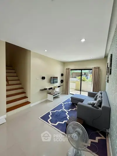 Modern living room with stylish decor and natural light, featuring a cozy sofa and elegant staircase.