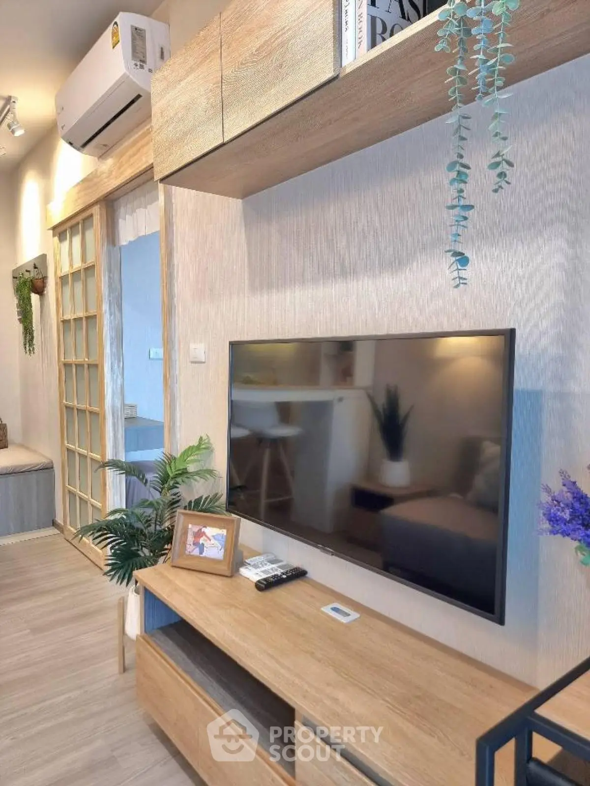 Modern living room with wooden furniture and wall-mounted TV, featuring stylish decor and air conditioning.