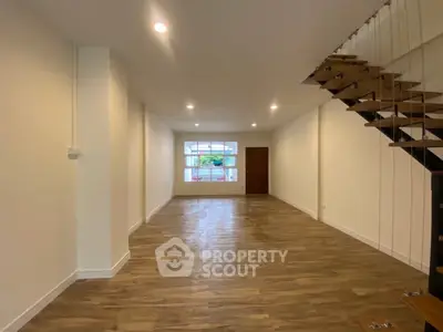 Spacious open-plan living room with modern staircase and large window view.