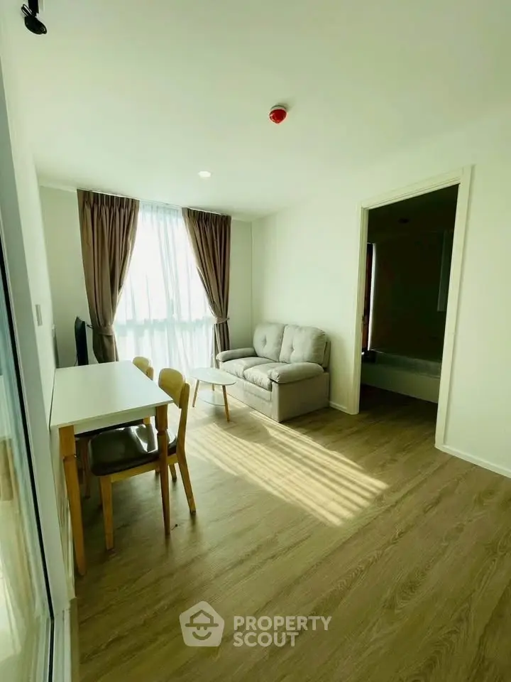 Bright living room with cozy sofa and dining area, featuring large window and wooden flooring.