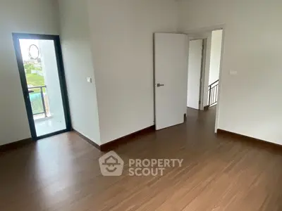 Spacious empty room with wooden flooring and balcony access in modern home