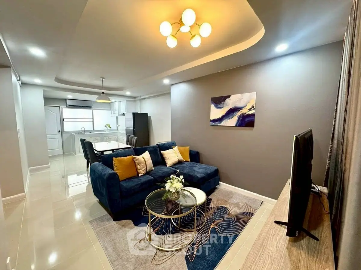 Modern living room with stylish decor and open kitchen layout, featuring a cozy blue sofa and elegant lighting.