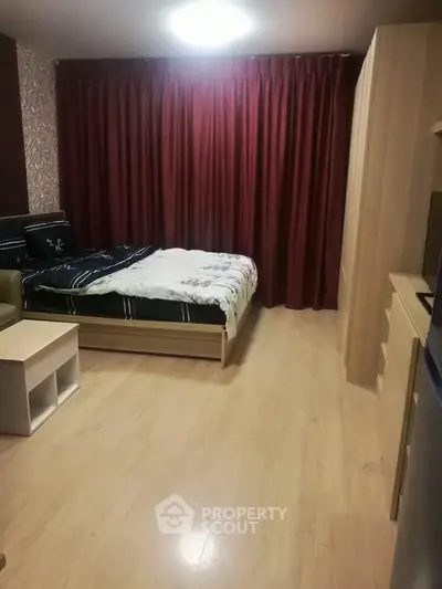 Cozy bedroom with wooden flooring and elegant red curtains, perfect for a restful retreat.