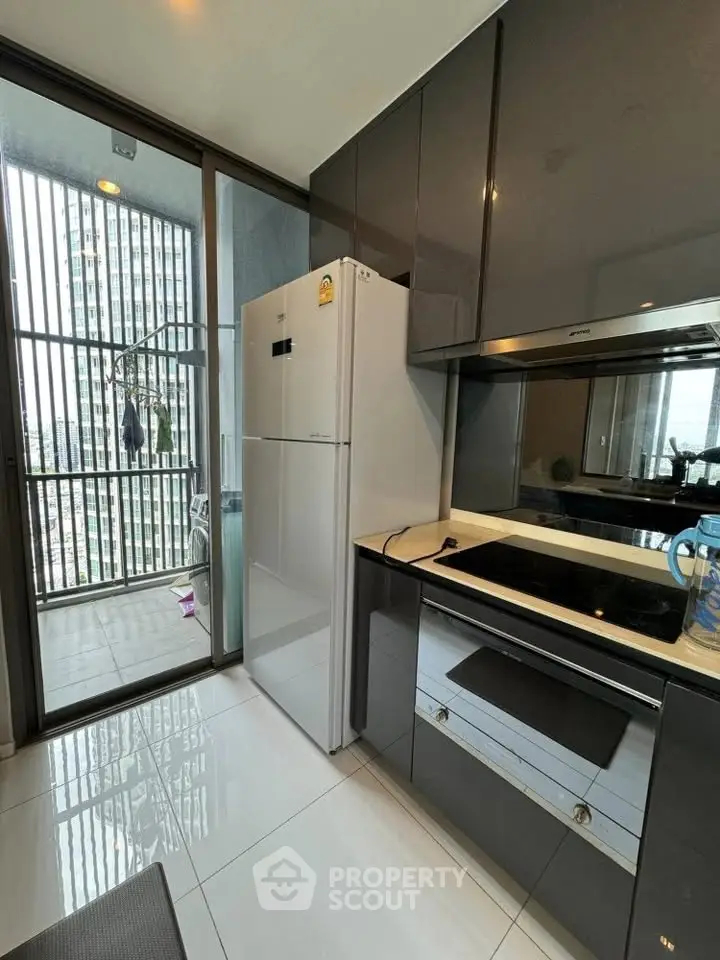 Modern kitchen with sleek cabinetry and balcony view, featuring built-in oven and spacious fridge.
